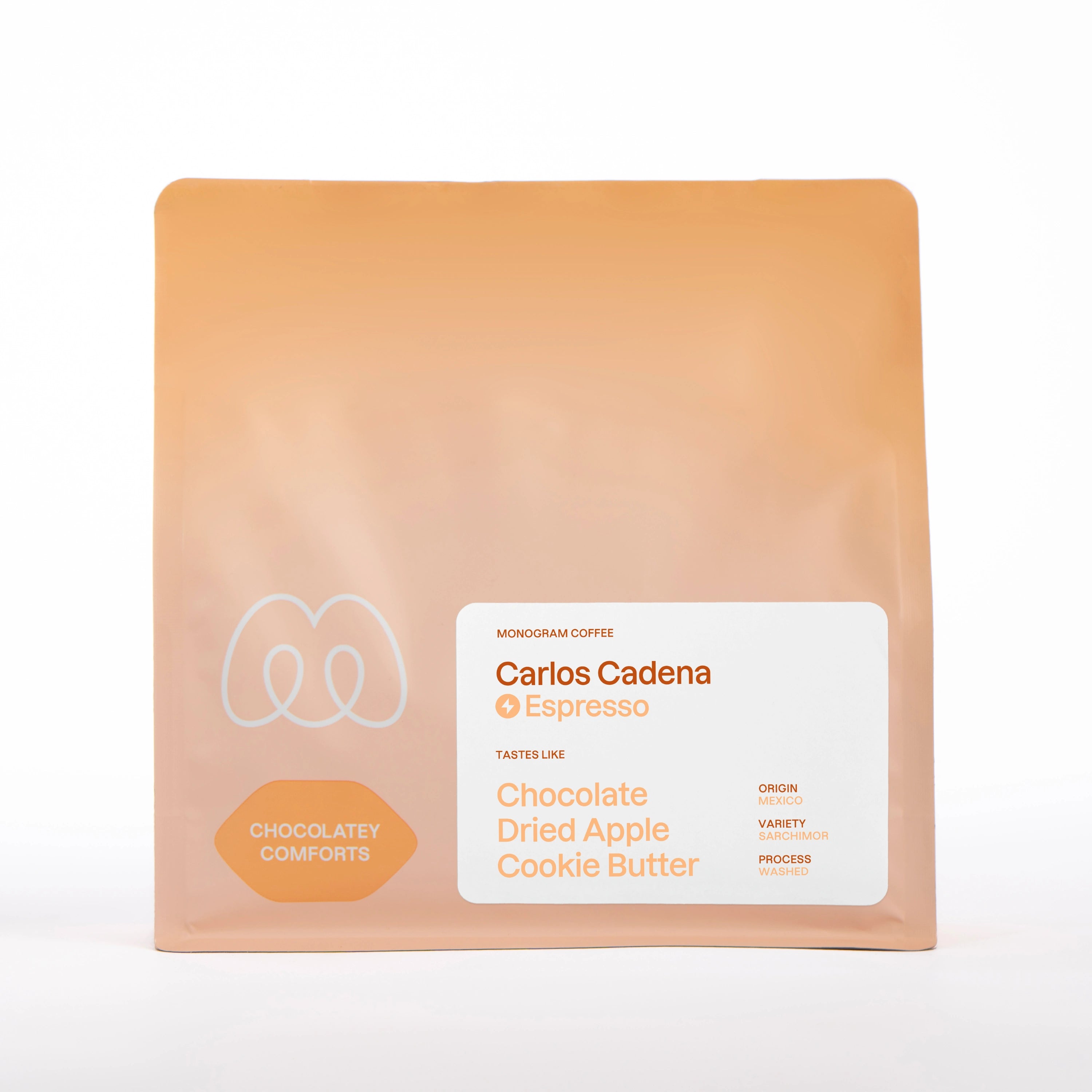 A warm beige, tan, and soft orange gradient bag of Monogram Carlos Cadena espresso coffee, a washed processed Sarchimor variety from Mexico with chocolatey comforts flavor profile and tasting notes of chocolate, dried apple, and cookie butter.