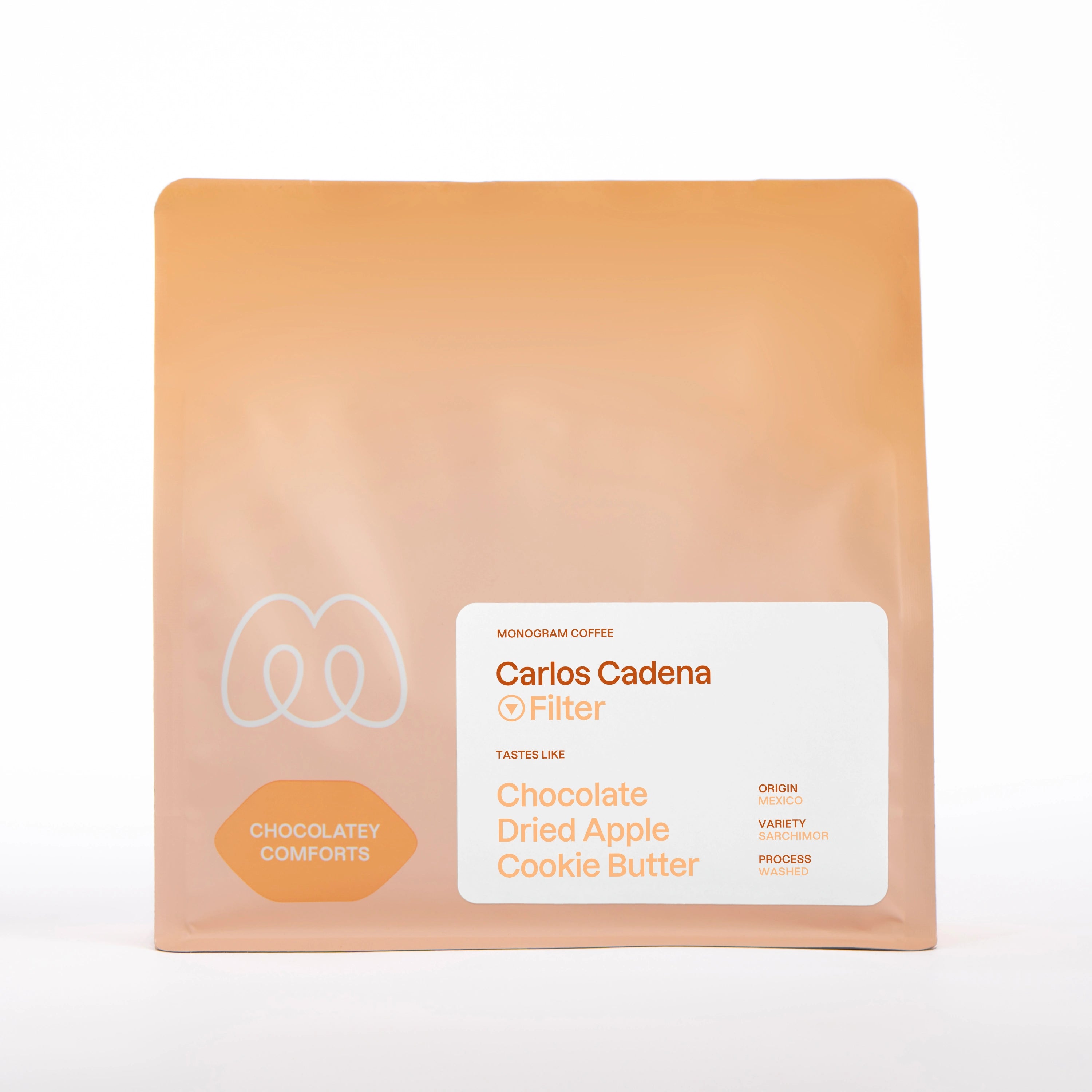 A warm beige, tan, and soft orange gradient bag of Monogram Carlos Cadena filter coffee, a washed processed Sarchimor variety from Mexico with chocolatey comforts flavor profile and tasting notes of chocolate, dried apple, and cookie butter.