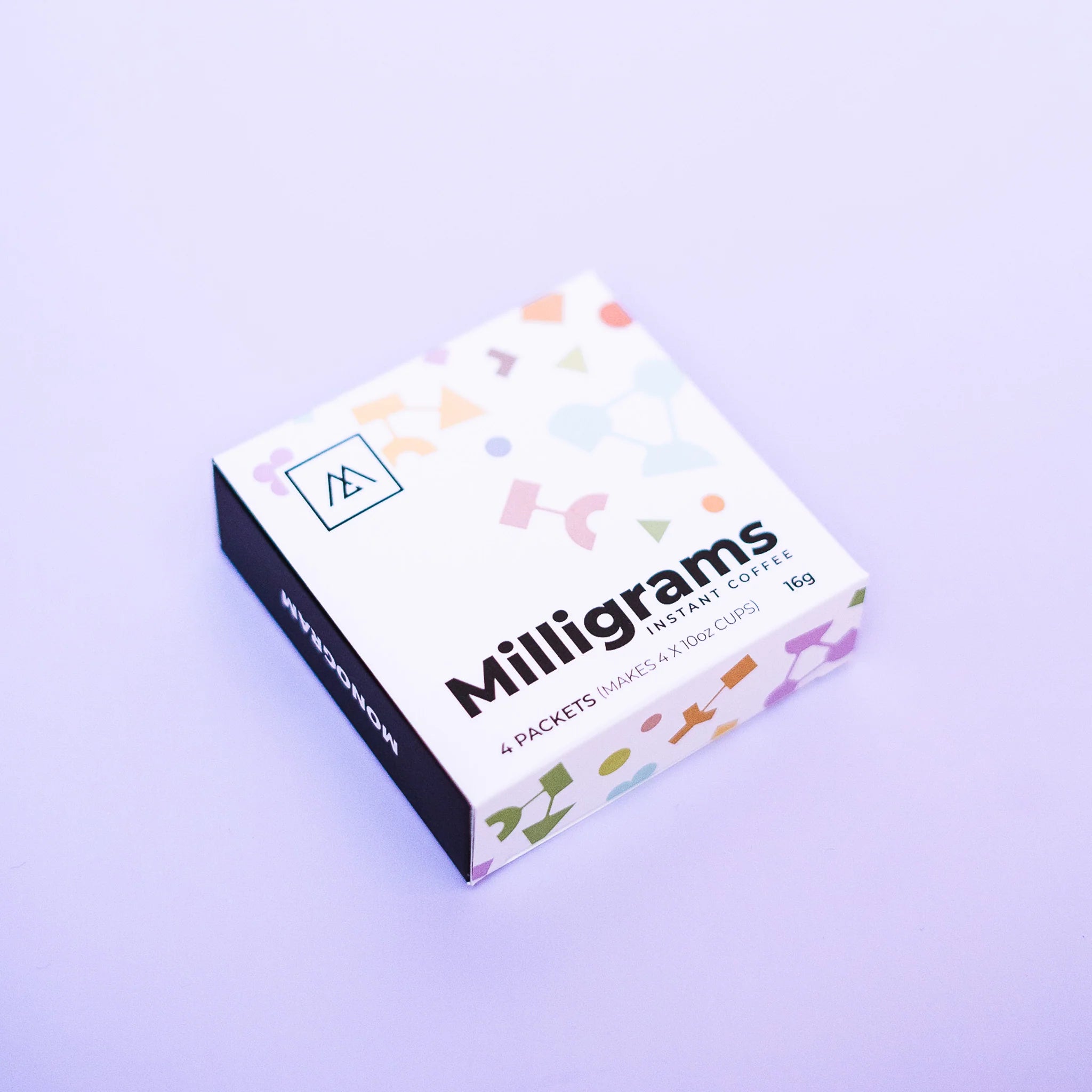 a box of Monogram Milligrams instant coffee crystals featuring a colorful geometric pattern, containing four packets of barista-quality specialty instant coffee.