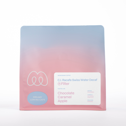 A blue and pink gradient bag of Monogram C.I. Racafe filter coffee, a Swiss Water Process decaf from Colombia (Washed Caturra and Castillo) with tasting notes of chocolate, caramel, and apple.