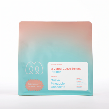 A peach and turquoise blue gradient bag of Monogram El Vergel Guava Banana filter coffee, a natural processed Red and Yellow Caturra variety from Colombia with a Super-Fruity Adventures label badge and tasting notes of guava, pineapple, and chocolate.
