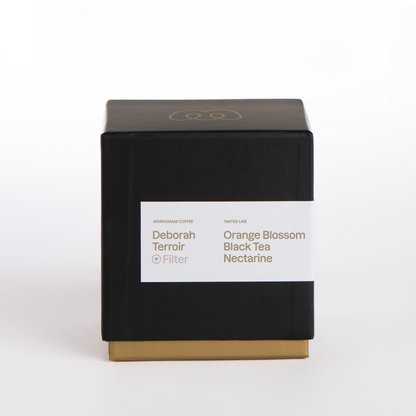 A premium black and gold box of Monogram Finca Deborah Terroir filter coffee, a washed Gesha from Panama with tasting notes of orange blossom, black tea, and nectarine.