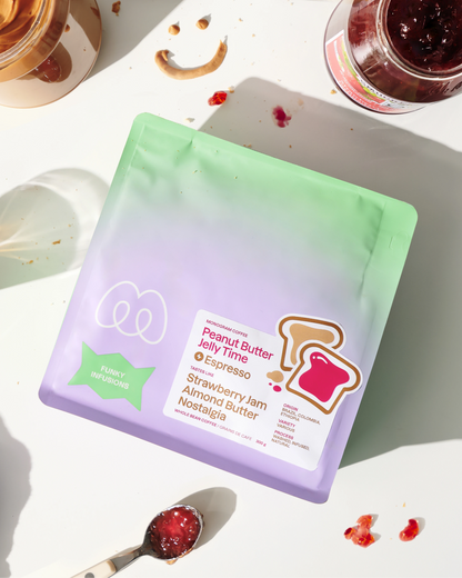 A purple and mint green gradient bag of Monogram Peanut Butter Jelly Time espresso coffee on a sunny table with almond butter, toast graphics, and a pink mug, featuring tasting notes of strawberry jam, almond butter, and nostalgia.