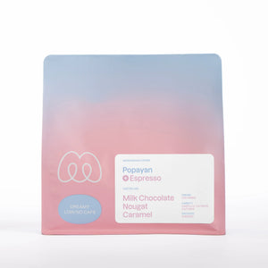 A blue and pink gradient bag of Monogram Popayan espresso coffee, a washed decaf from Colombia (Castillo, Catimor, and Caturra varieties) with tasting notes of milk chocolate, nougat, and caramel.