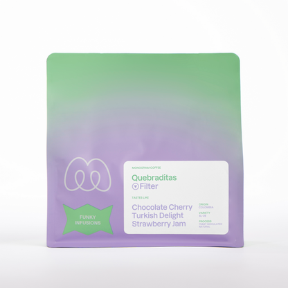 A purple and green gradient bag of Monogram Quebraditas filter coffee, a yeast inoculated natural SL-28 from Colombia with tasting notes of chocolate cherry, turkish delight, and strawberry jam.