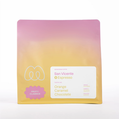 A pink and yellow gradient bag of Monogram San Vicente espresso coffee, a washed Caturra and Castillo variety from Huila, Colombia, with tasting notes of orange, caramel, and chocolate