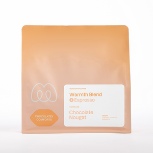 A peach-colored bag of Monogram Warmth espresso coffee blend from Central and South America, featuring tasting notes of chocolate and nougat.